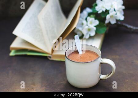 Eine gemütliche Ostern, Frühling Stillleben Szene. Eine Tasse Kaffee, ein Buch, ein blühender Ast eines Apfelbaums auf dunklem Grund. Vintage Foto im Damenstil,