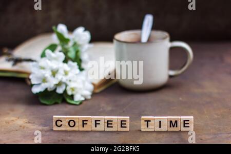 Frühlingsstill-Leben auf dunklem Hintergrund. Die Inschrift 'Coffee Time' EINE Tasse Kaffee, ein Buch, ein blühender Ast eines Apfelbaums. Vintage-Stil phot Stockfoto