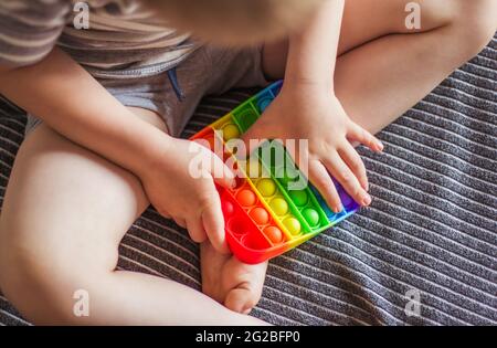 Blonde junge spielt mit Regenbogen Pop es fidget Spielzeug. Push Bubble Fidget Sinnesspielzeug - waschbares und wiederverwendbares Stressabbau-Spielzeug. Antistress-Spielzeug für Kinder Stockfoto