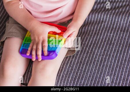 Ein kleines Mädchen sitzt und hält ein Spielzeug in ihren Händen Regenbogen Pop it Fidget Spielzeug. Push Bubble Fidget Sinnesspielzeug Silikon Stress Relief Spielzeug. Anti-Stress-Spielzeug für Stockfoto