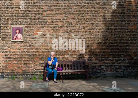Frau, die in blauer Kleidung auf einer Bank sitzt und im öffentlichen Raum mit einem Mobiltelefon gegen eine Ziegelmauer in Beverley, Yorkshire, Großbritannien, spricht. Stockfoto