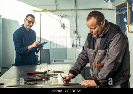 Ein Kinnschmied skizziert in der Werkstatt und er berät sich mit einem Kollegen Ingenieur, der Notizen macht. Stockfoto