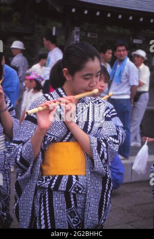 TOKIO, JAPAN - 04. Jun 2021: Japanisches Mädchen in blauem Kimono und gelber Schärpe spielt auf einer japanischen Straße in Tokio Flöte. Stockfoto