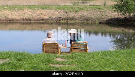 Rückansicht von lustigen glücklichen kaukasischen älteren Frauen in Hüten, die in einem Park in der Nähe des Flusses ruhen. Sie reden und genießen die Natur. Menschen von Happines Stockfoto