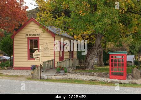 Historische Architektur in der Kleinstadt Cardrona, Neuseeland. Das Old School House (Ende des 19. Jahrhunderts), jetzt eine Galerie und eine retro-rote Telefonbox Stockfoto