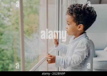 Süßes afroamerikanisches Kind, das durch das Fenster schaut und auf die Eltern wartet Stockfoto