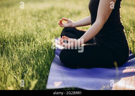 Die junge kaukasische Frau praktiziert Yoga in Lotusstellung an einem frühen sonnigen Morgen in einem Wald. Gesundes Lifestyle-Konzept. Morgenmeditation, relaxati Stockfoto