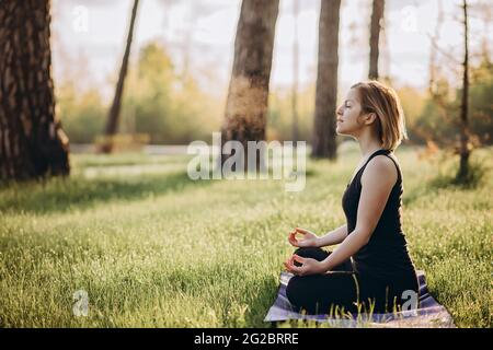 Eine junge kaukasische Frau praktiziert Yoga an einem frühen sonnigen Morgen im Wald zwischen den Bäumen. Gesundes Lifestyle-Konzept. Morgenmeditation Stockfoto