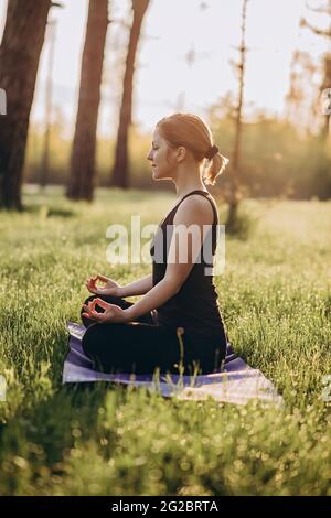 Eine 36-jährige junge Frau praktiziert Yoga an einem Morgen im Wald zwischen den Bäumen in der Lotusposition. Gesundes Lifestyle-Konzept. Morgenmeditati Stockfoto