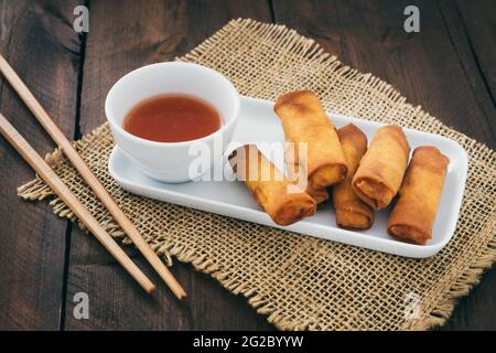 Mini-Frühlingsrollen mit süß-würzigem Dip und Essstäbchen auf Ein rustikaler Holztisch Stockfoto