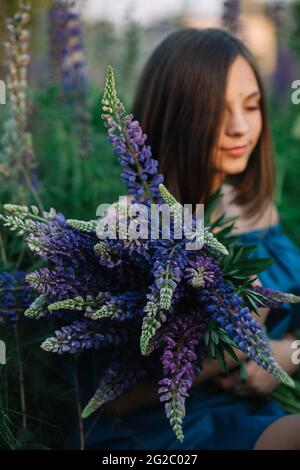 Junge schöne Mädchen in Unschärfe mit einem großen Bouquet von lila Lupinen in einem Feld im Gras. Naturkonzept. Nahaufnahme. Stockfoto