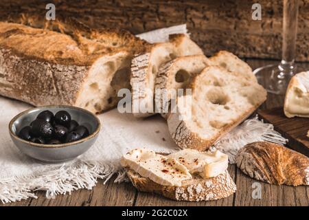 Knuspriges französisches Weißbrot mit Käse und Oliven auf rustikalem Holztisch Stockfoto