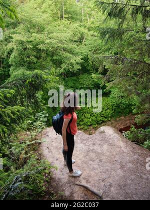 Ein Mädchen mit Rucksack steht am Rand einer Klippe. Reisen Sie außerhalb der Stadt im Wald. Camping. Stockfoto