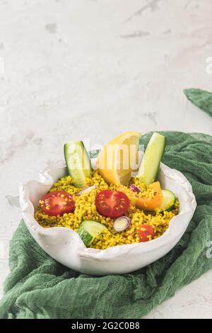 Couscous-Salat mit Gurken, Tomaten und Zwiebeln in einer weißen Schüssel auf weißem Hintergrund, vertikal mit Kopierfläche Stockfoto