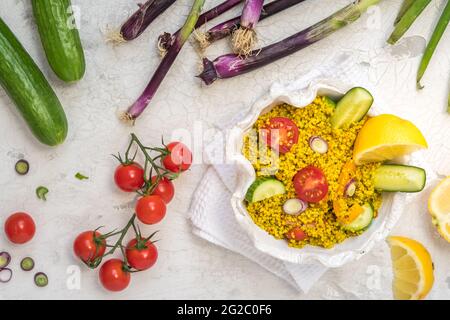 Gesunder Couscous-Salat mit Gurken, Tomaten und Zwiebeln in einer weißen Schüssel auf weißem Hintergrund, verziert mit buntem Gemüse, Draufsicht Stockfoto