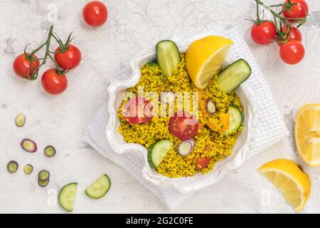 Gesunder Couscous-Salat mit Gurken, Tomaten und Zwiebeln in einer weißen Schüssel auf weißem Hintergrund, Draufsicht Stockfoto