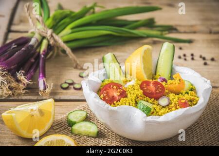 Couscous-Salat mit Gurken, Tomaten und Zwiebeln in einer weißen Schüssel auf rustikalem Holzhintergrund Stockfoto
