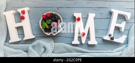 Das Wort Home in weißen Buchstaben auf blauem Hintergrund, verziert mit frischen Beeren, Konzept für den Aufenthalt zu Hause, zum Beispiel während der Covid-19 Pandemie Stockfoto