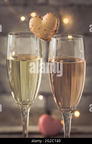 Zwei Gläser mit Sekt und herzförmigen Makronen auf einem rustikalen Holztisch, romantische Atmosphäre, vertikal Stockfoto