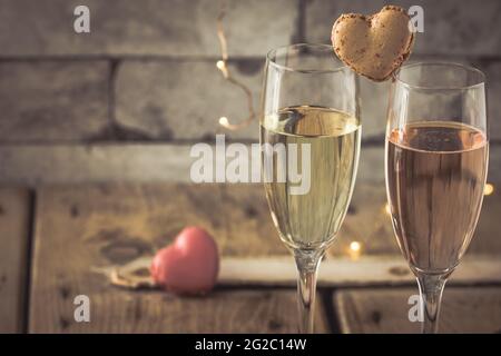 Zwei Gläser mit Sekt und herzförmigen Makronen auf einem rustikalen Holztisch, romantische Atmosphäre Stockfoto