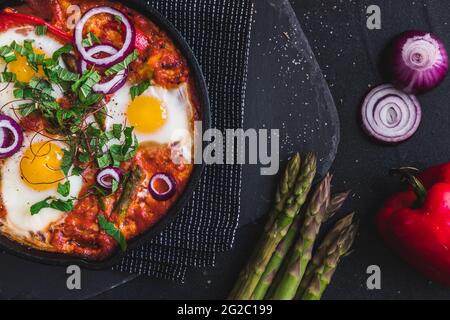 Shakshuka in einer Eisenpfanne. Traditionelles Gericht aus dem Nahen Osten. Spiegeleier mit Tomaten, Paprika, Gemüse und Kräutern, Spiegeleier in sonniger Lage. Draufsicht. Stockfoto