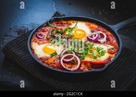 Shakshuka in einer Eisenpfanne. Traditionelles Gericht aus dem Nahen Osten. Spiegeleier mit Tomaten, Paprika, Gemüse und Kräutern, Spiegeleier in sonniger Lage. Speicherplatz kopieren Stockfoto