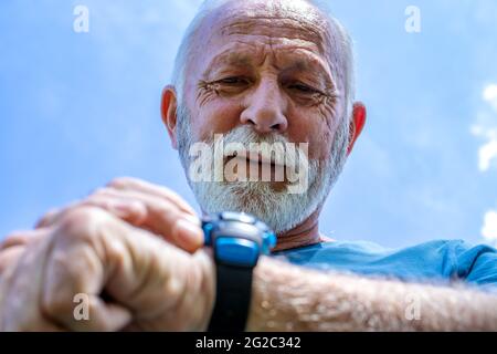 Porträt eines älteren Mannes, der seine Uhr überprüft.der ältere Sportler, der seine Herzfrequenz und seinen Blutdruck durch die Überwachung seiner Smartwatch kontrolliert. Stockfoto