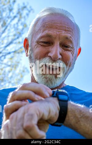 Porträt eines älteren Mannes, der seine Uhr überprüft.der ältere Sportler, der seine Herzfrequenz und seinen Blutdruck durch die Überwachung seiner Smartwatch kontrolliert. Stockfoto