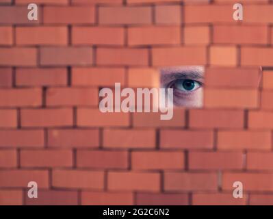 Verdächtige Person, die durch das Loch in der Ziegelwand schaut. Konzept von Spionage, Spionage und Peeking Stockfoto