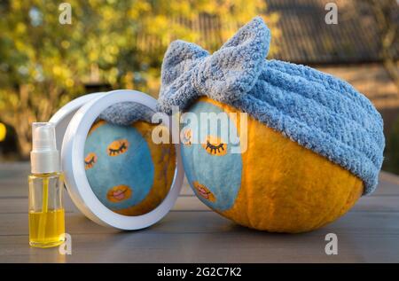 Großer orangefarbener Kürbis mit bemalten Augen, Lippen und einer Tonmaske vor einem Spiegel. Genießt Schönheitsbehandlungen. Humor Beauty Konzept. Selbstbestimmt Fokus. Au Stockfoto