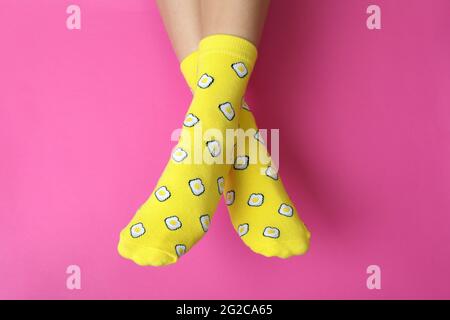Weibliche Beine in lustigen Socken auf rosa Hintergrund Stockfoto