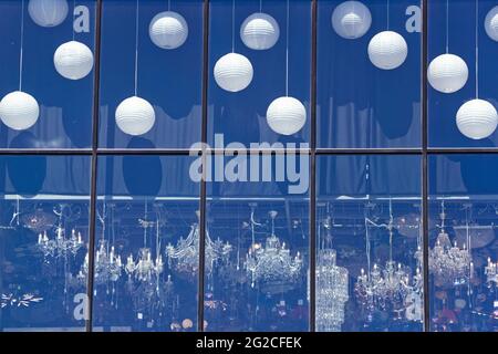 Kaufen Sie eine Leuchtenvitrine mit Kronleuchtern. Blick auf die Straße vom Fenster. Eine Auswahl an Kronleuchtern verschiedener Art im Laden. Stockfoto
