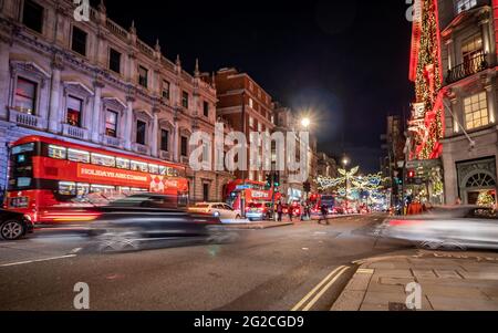 Piccadilly, London. Weihnachtsansicht des exklusiven Londoner Viertels Piccadilly mit starkem Verkehr, der den festlichen Nachtlichtern Farbe verleiht. Stockfoto
