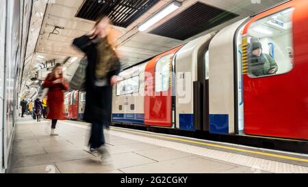 U-Bahn London. Lange Belichtungszeit verwackelte Passagiere, die den Bahnsteig einer U-Bahnstation mit einem Zug am Bahnsteig verlassen. Stockfoto