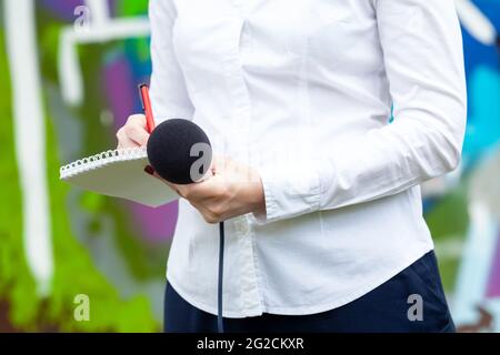 Nachrichtenreporter oder Fernsehjournalist bei der Pressekonferenz, hält Mikrofon und schreibt Notizen Stockfoto