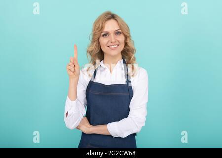 Inspirierte Frau in Schürze Zeigefinger. Hausfrau drücken Glück. Positive Emotionen. Stockfoto