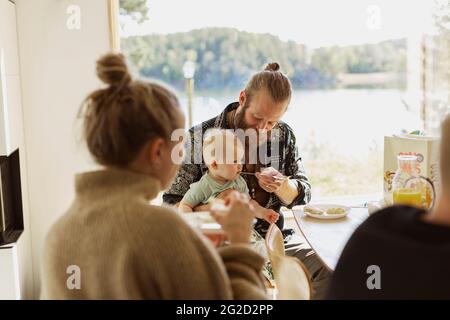 Mann, der während des Frühstücks einen kleinen Sohn füttert Stockfoto