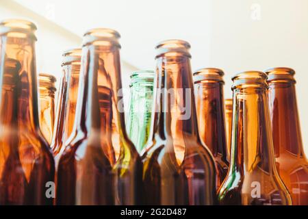 Eine leere grüne Glasflasche, umgeben von anderen braunen Flaschen, die aus einem niedrigen Winkel gesehen werden. Viel Licht dringt hinter die Flaschen ein.