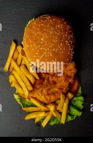 Vertikaler Schuss eines leckeren Hähnchenburger mit Pommes auf einer dunklen Oberfläche Stockfoto