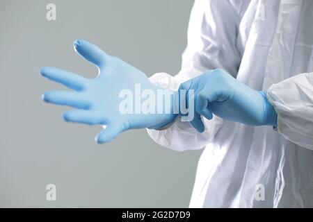 Der Arzt in einem Schutzanzug zieht blaue Gummihandschuhe an Stockfoto