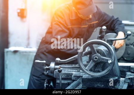 Nicht erkennbarer unscharfer Arbeiter in Uniform bei der Arbeit mit Metallbearbeitungsmaschine. Stockfoto