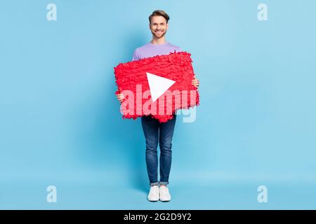 In voller Länge Foto zufrieden freundlich Kerl Arme halten große Play-Taste Collage isoliert auf blauem Hintergrund Stockfoto