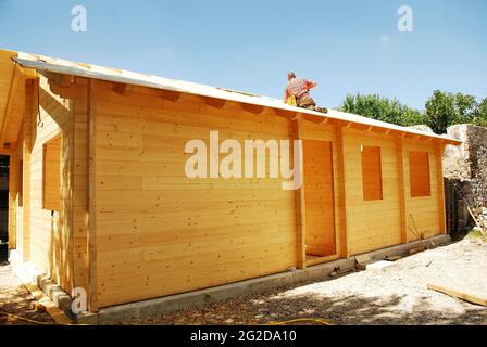 Ein teilweise gebautes Holzhaus (Tanne) auf einer inländischen Baustelle. Die Hintertür ist hier zu sehen, und ein Baumeister ist auf dem Dach Stockfoto