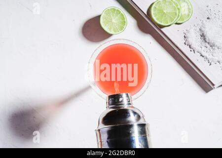 Paloma-Cocktail mit Salzbemalung, Tequila und Grapefruitsaft, Limettenscheibe auf weißem Tisch garniert. GLA mit saftigem Fruchtcocktail aus dem Shaker füllen Stockfoto