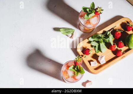 Erfrischender Sommerdrink Caipirinha Cocktail mit Erdbeeren und frischer Minze in Gläsern, hartes Licht mit Schatten Stockfoto