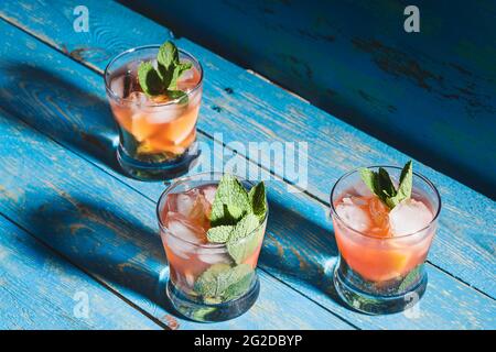 Eiskalte hausgemachte Zitronensaftgetränke mit frischen Erdbeeren und Minze, Limonade in Gläsern auf rustikalem blauen Holztisch Stockfoto