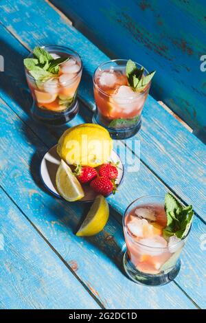 Eiskalte hausgemachte Zitronensaftgetränke mit frischen Erdbeeren und Minze, Limonade in Gläsern auf rustikalem blauen Holztisch Stockfoto