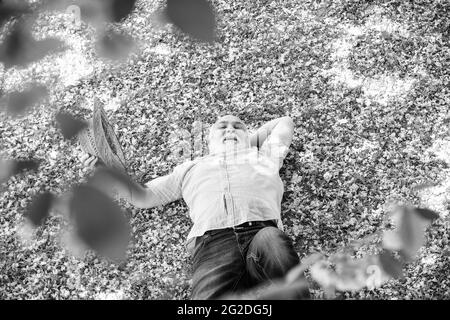 Angenehmer Frühlingstag. Mann unter kirschblühenden Baum. Alter Mann genießen Frühlingscharakter. Älterer Mann mit grauem Bart im Strohhut. Glücklicher Ruhestand Stockfoto