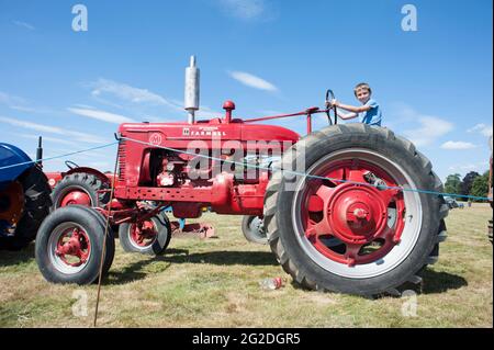 Ein kleiner Junge sitzt auf einem leuchtend roten, restaurierten landwirtschaftlichen Traktor im Vintage-Stil bei einer Country Show Stockfoto