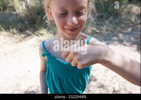 Ein Schmetterling landet auf der Hand eines jungen Mädchens, während sie in der Natur spazieren geht. Stockfoto